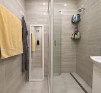 Bathroom in a studio apartment with a glass shower enclosure and light tiles.