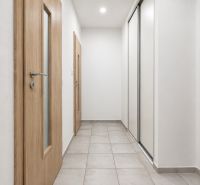 A hallway with tiles in a studio apartment, wooden doors, and white wardrobes.
