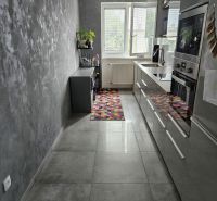 A kitchen with gray walls and flooring in a 4-room apartment, a colorful rug by the window.