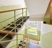 A bright stairway corridor with wooden railing and a view of greenery.