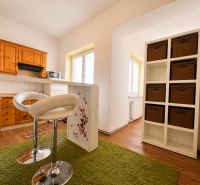 A kitchen in a studio apartment with cabinets, bar stools, and a wood-patterned floor.