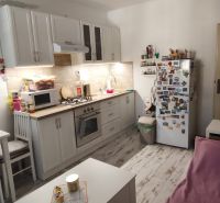 A kitchen in a studio apartment with white furniture and a wood-patterned floor.