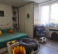 A bedroom in a studio apartment with a bed, a desk, and a wooden floor.