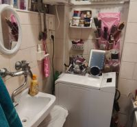 Compact bathroom with a washing machine, sink, and storage spaces in a studio apartment.