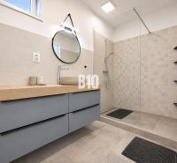 Interior of a holiday apartment with a modern bathroom, shower cabin, and round mirror.