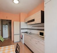 A kitchen with orange walls, cabinets, and white appliances in a 3-room apartment.