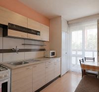 A kitchen in a 3-room apartment with a wooden decor floor and balcony doors.