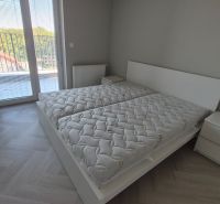 A bedroom in a three-room apartment with a wood-patterned floor and a large window.