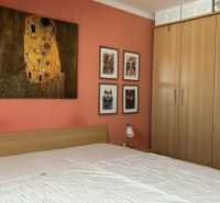 A bedroom in a 4-room apartment with an orange wall, paintings, and a wooden wardrobe.