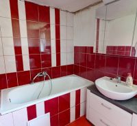 A bathroom in a family house with red and white tiles, a bathtub, and a sink.