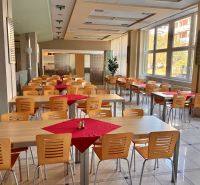 A bright office canteen with wooden tables, chairs, and large windows.