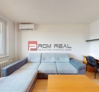 Living room with a sofa and a desk in a 3-room apartment with wood-patterned flooring.
