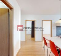 Interior of a 3-room apartment with a wooden decor floor, a table, and red chairs.