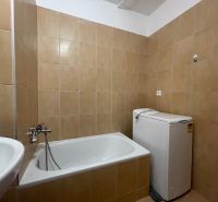 Bathroom with a bathtub and a washing machine in a 2-room apartment. Tiled walls, white sanitary equipment.