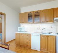 A kitchen with wooden cabinets, a microwave, and a view into the living room in a 3-room apartment.