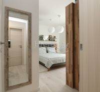 Bedroom in a vacation apartment with a mirror and a bed, floor with wood decor.