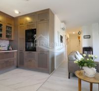 A kitchen in a holiday apartment with an open living room, wooden cabinets, and light flooring.