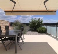 The terrace of the recreational apartment in Tribunj with spacious seating and an awning, surrounded by greenery.