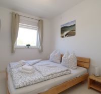 Bright bedroom in a holiday apartment with a double bed and a TV on the wall.