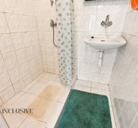 A bathroom in a family house with a sink and a shower, tiled with white tiles.
