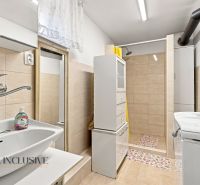 Bathroom with a sink, shower, and washing machine in a family house, with tiles and light-colored tiles.