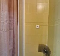 A shower corner in the bathroom of a 3-room apartment with beige tiles and a curtain.
