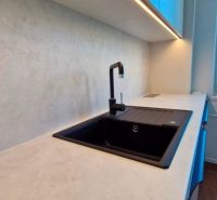 A kitchen in a 3-room apartment with a white countertop and a black sink.