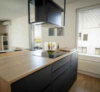 A kitchen in a 3-room apartment with a wooden decor floor and black cabinets.