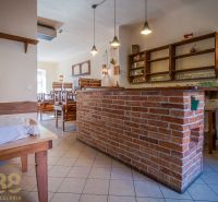 Interior of a gastro space with a brick bar, wooden chairs, and a tiled floor.