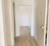 A hallway with white walls and a wooden decor floor in a 3-room apartment.