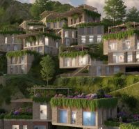 A complex of multiple villas set into the hillside in Dhërmi, surrounded by lush vegetation.