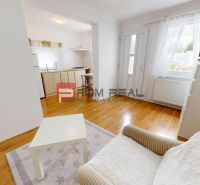 Living room of a one-bedroom apartment with a wooden decor floor, television, and kitchenette.