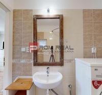 A bathroom in a studio apartment with a sink, a washing machine, and a mirror on the wall.