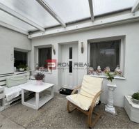 Covered terrace with white furniture and decorations by a studio apartment.