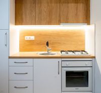 A kitchenette in a studio apartment with a wood decor, white cabinets, and a gas stove.