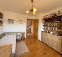 Interior of a family house with wooden decor, shelves with decorations, and a simple bed.