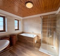 A bathroom with a bathtub, shower, and wooden decor flooring in a family house.