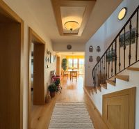 A hallway in a family house with a staircase, wall decorations, and a wooden-patterned floor.