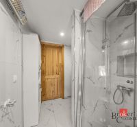 A bathroom with ceramic tiles, a glass shower enclosure, and wooden doors in a family house.