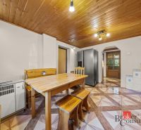 Dining room in a family house with a wooden ceiling, table and bench, tiled floor with a geometric pattern.