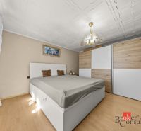 Bedroom in a family house with a bed, wardrobe, and wooden decor flooring.