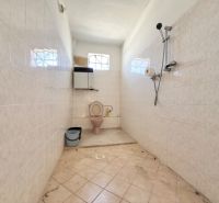 Bathroom with toilet, shower, and bucket, tiled walls, family house.