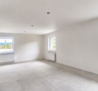 A spacious room in a family house with white walls and large windows.