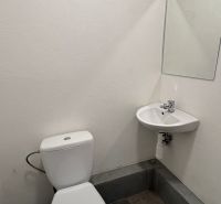 A restroom with a sink in commercial premises, white walls, dark tiles.