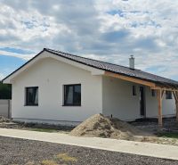 A family house in Bellova Ves with a white facade, a sloped roof, and surrounding buildings.