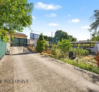 Access road to a residential plot in the town of Pezinok surrounded by greenery and a fence.