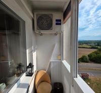 A narrow balcony in a 3-room apartment with a sofa and air conditioning, overlooking nature.