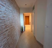A hallway in a 3-room apartment with a stone decor on the wall and tiles on the floor.