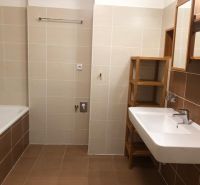 A bathroom in a 2-room apartment with light tiles, a bathtub, and a sink.