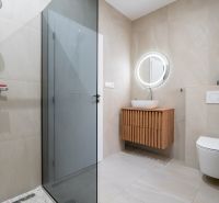 A bathroom in a family house with a sink, a shower, and a backlit mirror.